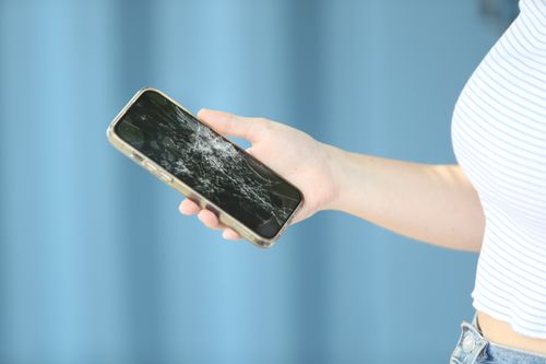 A person holding a phone with a broken screen