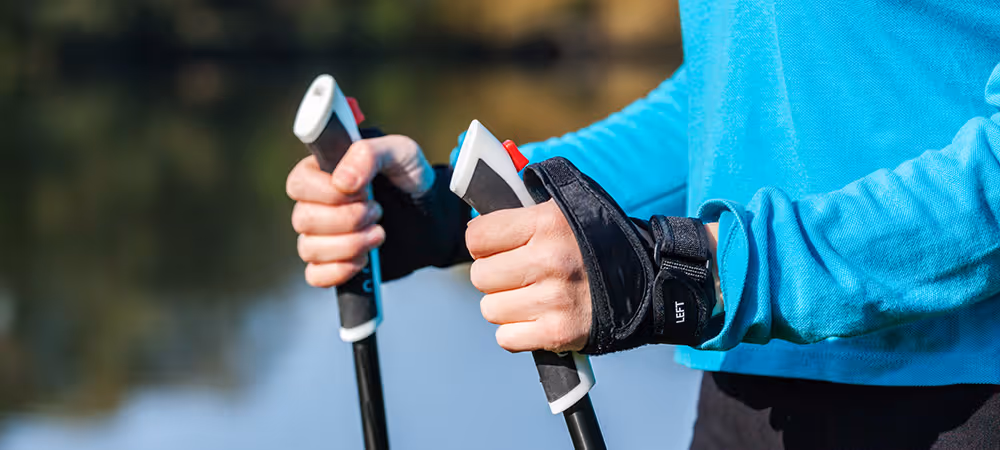 Ein Therapeut hält 2 Nordic Walking Stöcke in der Hand. Wir sehen eine Großaufnahme vom oberen Teil der Stöcke in der Hand.