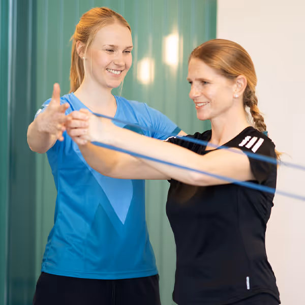 Physiotherapeutin der Rheinblick Physio trainiert mit Patientin, die eine Rückenübung mit dem Theraband durchführt.