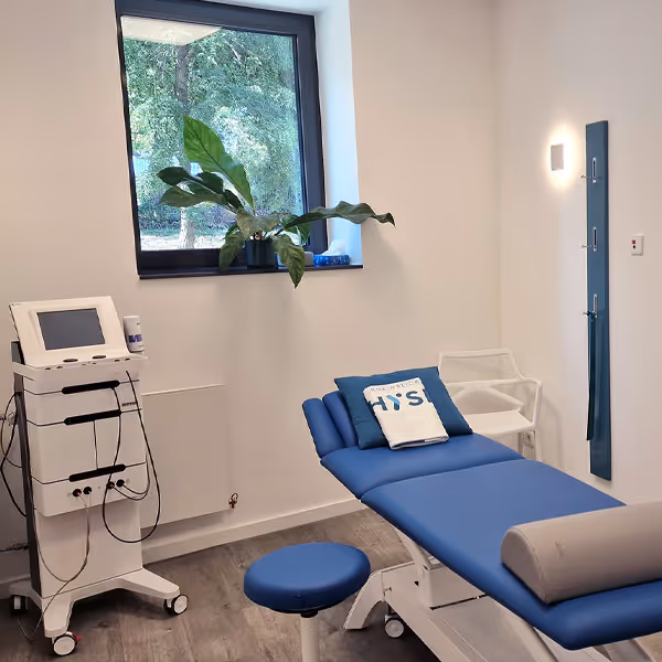Behandlungsraum der Rheinblick Physio mit Behandlungsliege, Elektrotherapiegerät und Blick durchs Fenster ins Grüne.