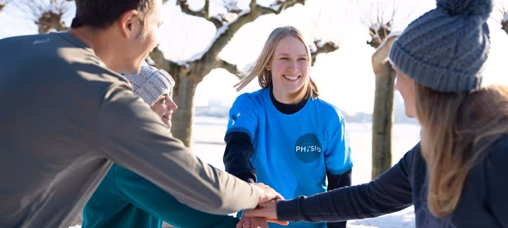 Die Physiotherapeutin von Rheinblick Physio lächelt und hält die Hände zusammen mit den Teilnehmern des Funktional Fit Kurses im Außenbereich.