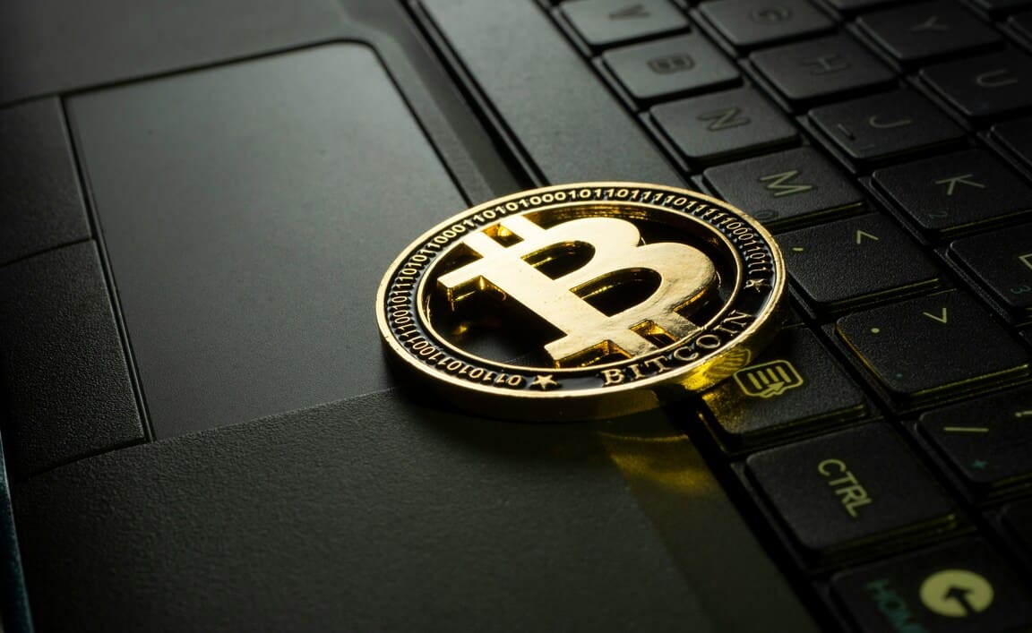 Auf einem Laptop liegt eine goldene Bitcoin-Münze.