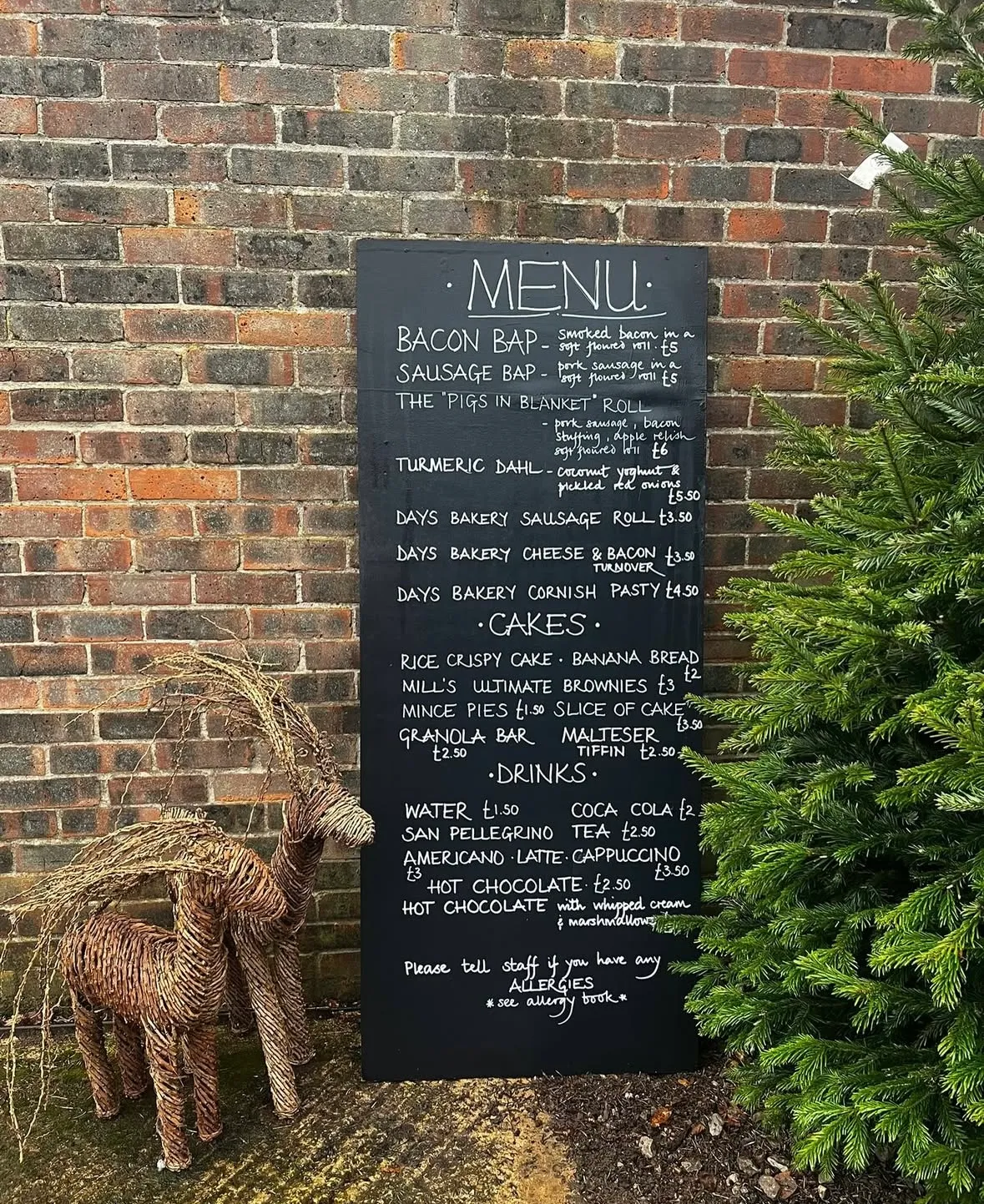 Christmas Cafe chalkboard menu against a brick wall, beside a wicker reindeer and a Christmas tree