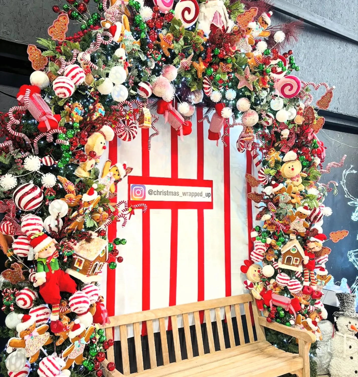 Festive archway covered in candy cane, gingerbread and bauble decorations above a wooden bench