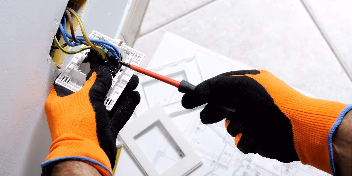 Intervention d’un électricien sur une prise murale avec des gants isolants et des outils de sécurité
