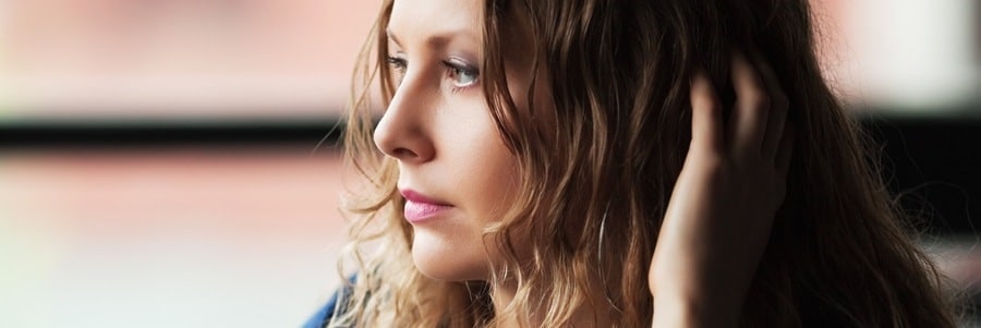 Woman looking contemplative, hand touching hair.