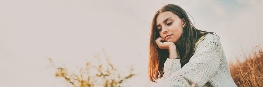 Woman sitting outdoors, looking pensive.