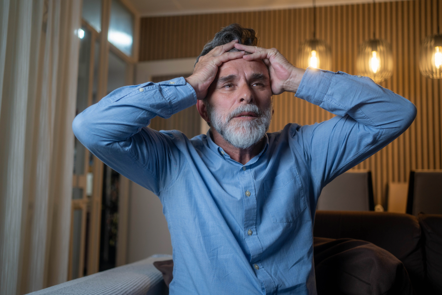 Older man in distress, hands on head, indoors.