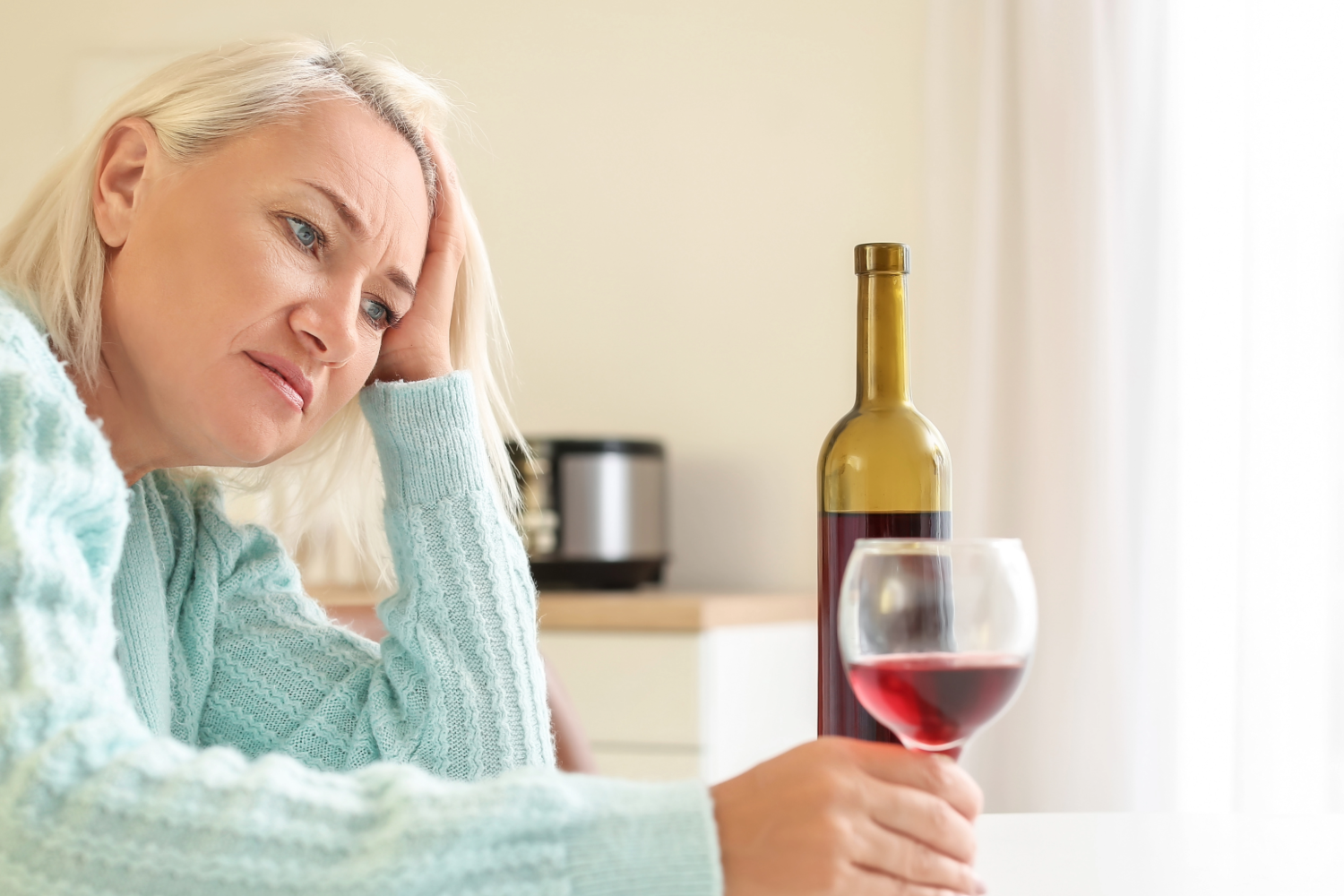 Pensive woman holding wine glass, bottle nearby.