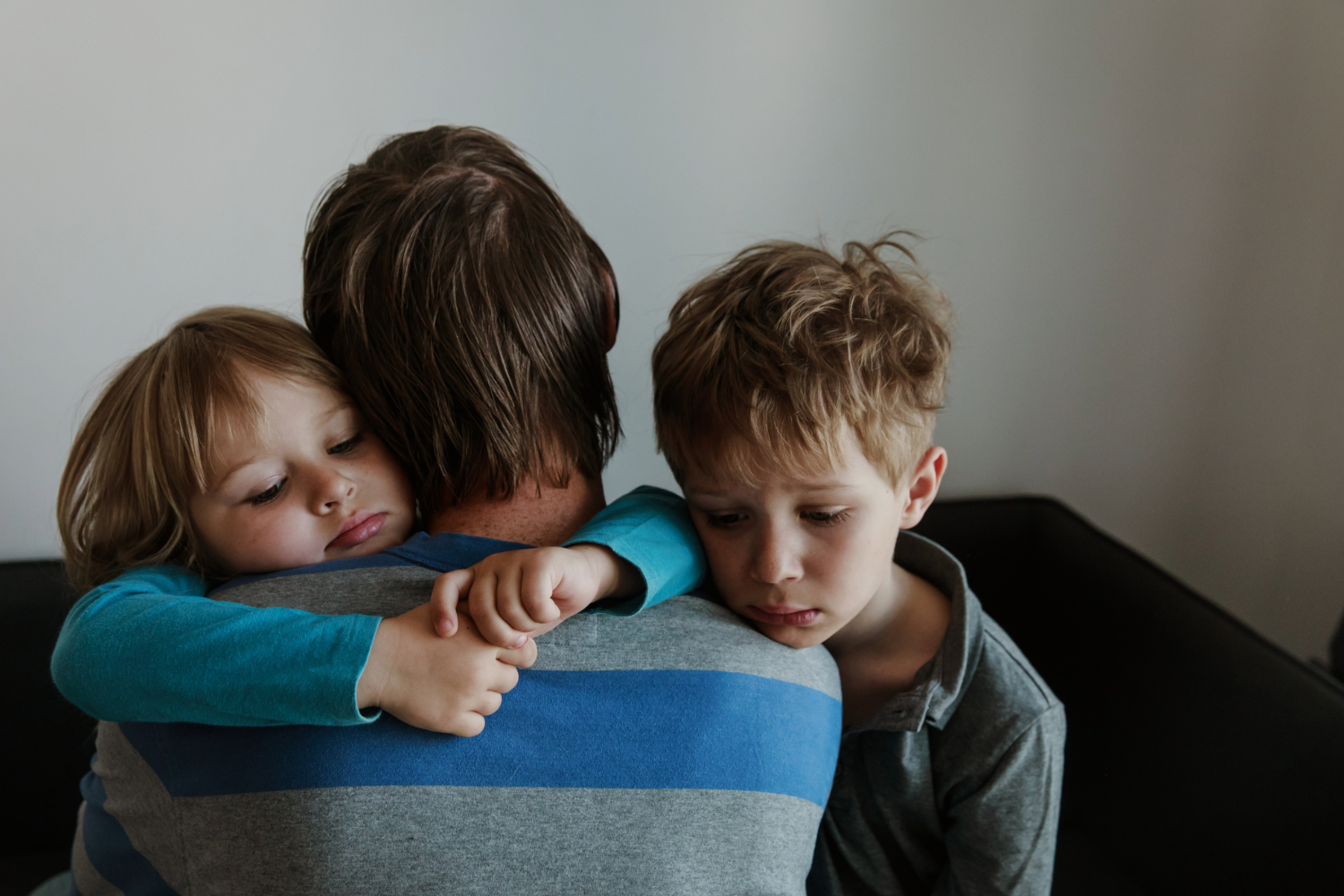 Parent hugging two children, comforting.