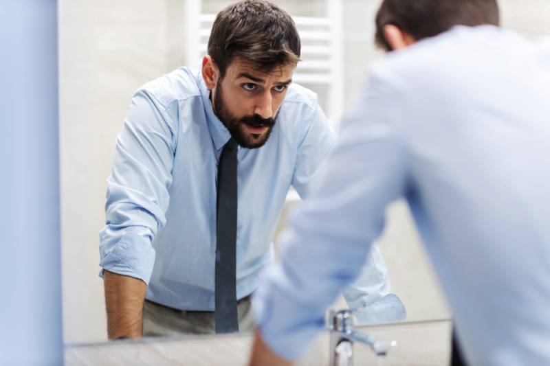 Man in tie looking at mirror, pensive expression.