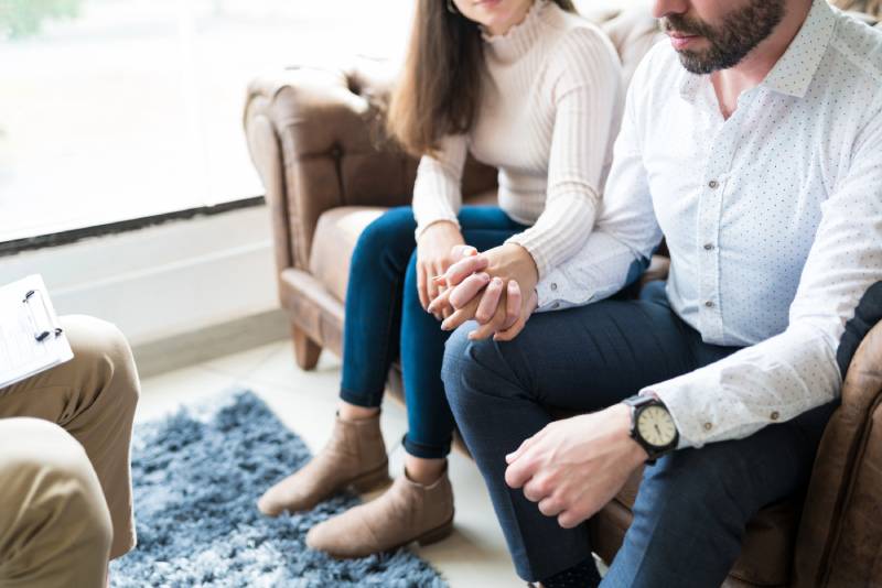 Couple holding hands on therapist's couch.