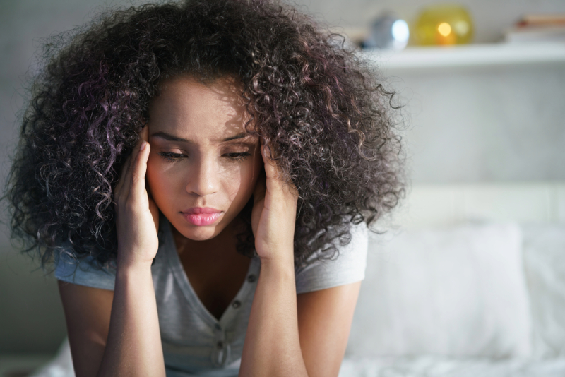 Stressed woman holding head in hands on bed.