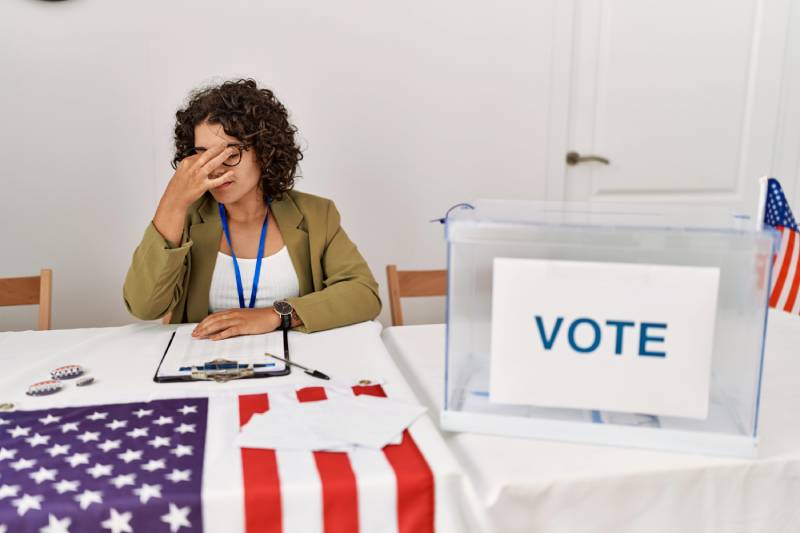 Stressed woman at voting station with USA flag.