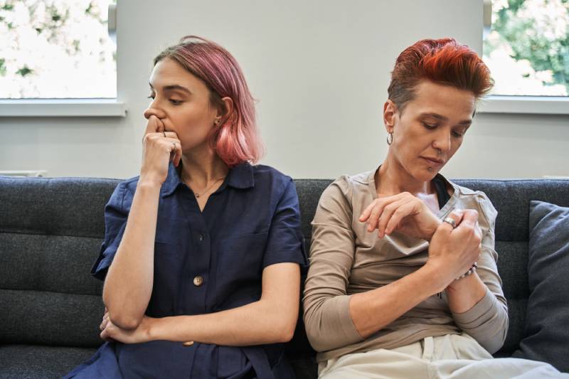 Two women with serious expressions sitting on a couch.
