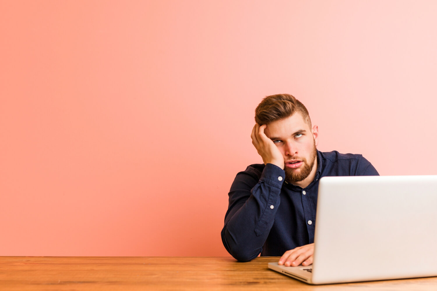 Man bored at laptop, pink background