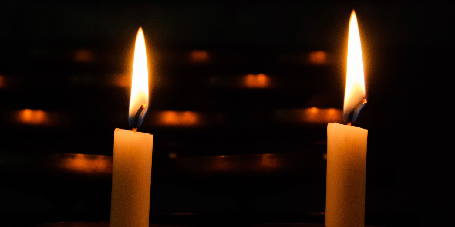 Two lit candles with dark background.