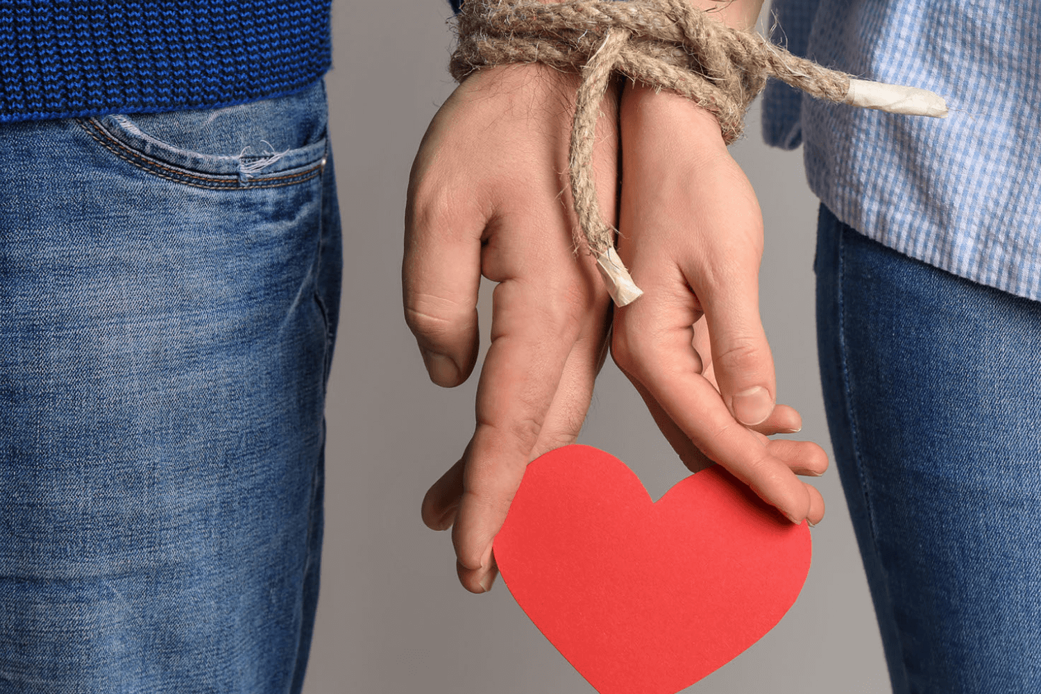 Hands tied with rope holding a red heart.