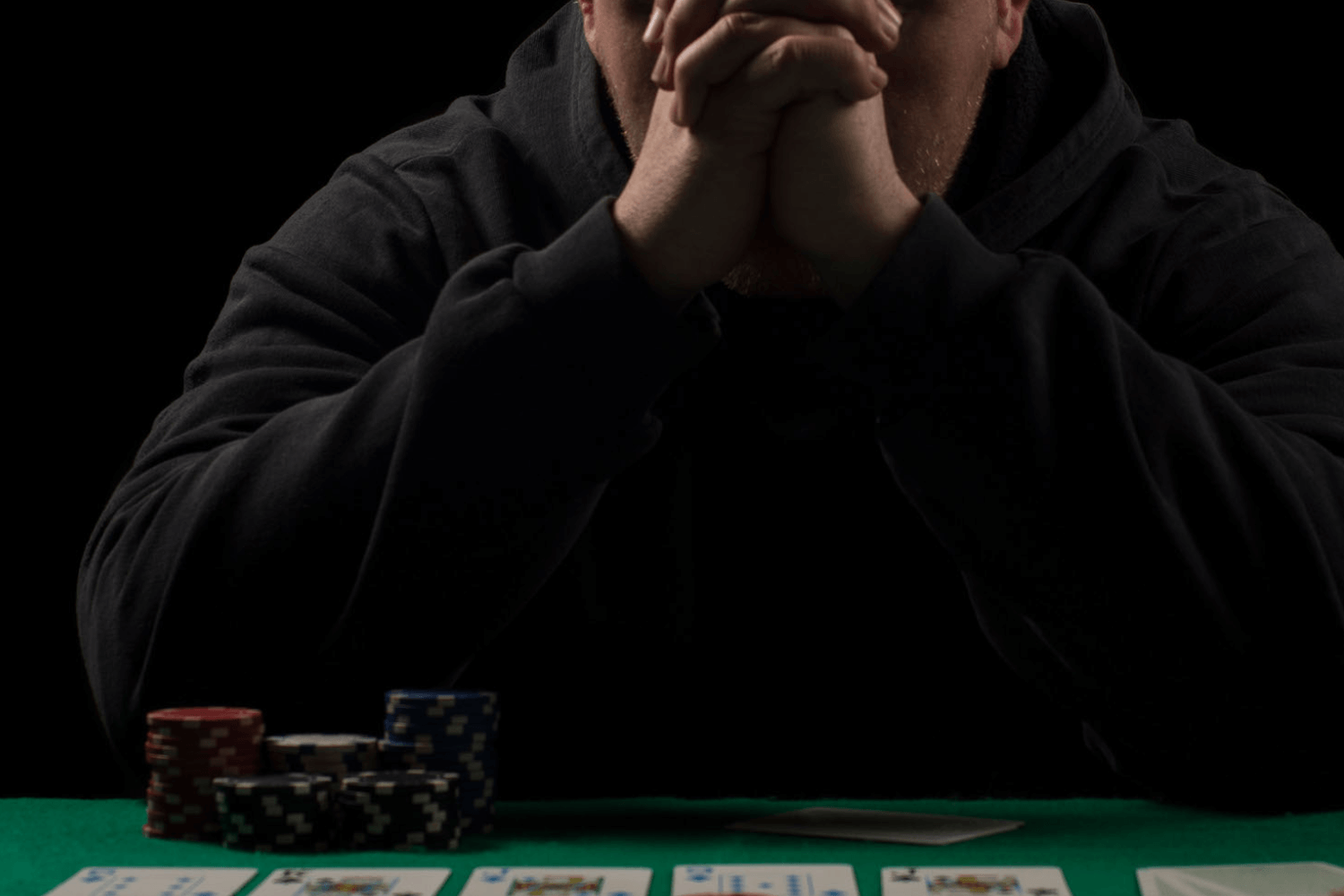 Man in hoodie at poker table with cards and chips