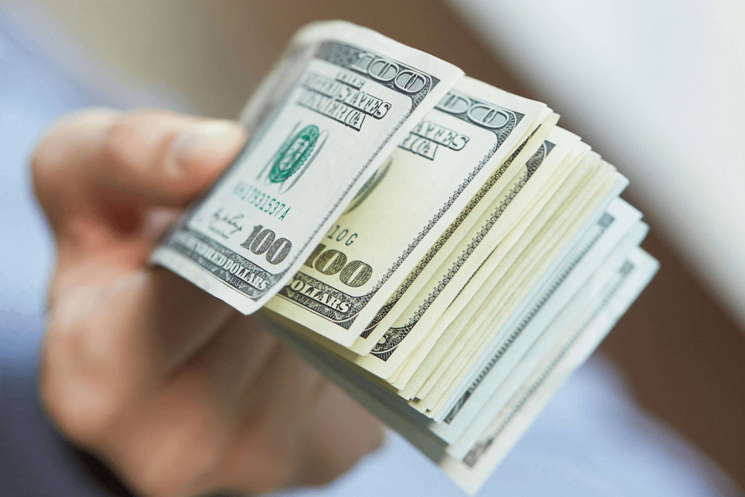 Hand holding stack of hundred-dollar bills.