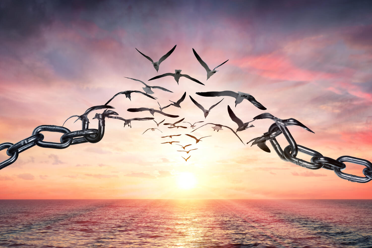 Birds flying through broken chains at sunset over ocean.