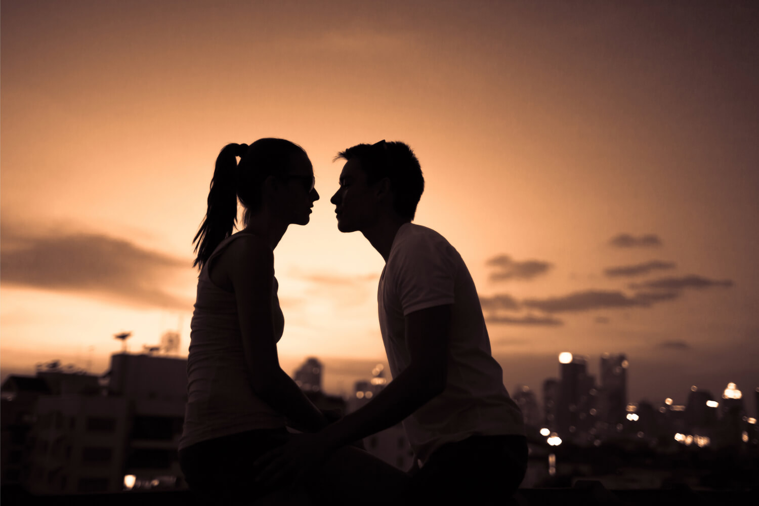 Silhouetted couple about to kiss at sunset.