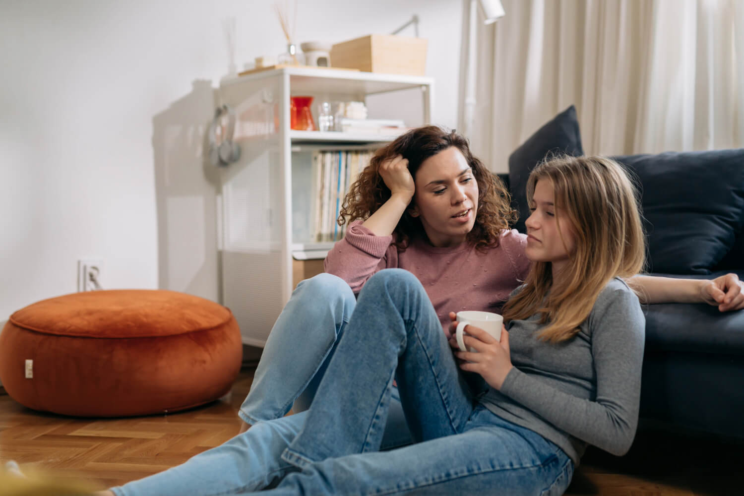 Mother and teenage daughter talking on living room floor.