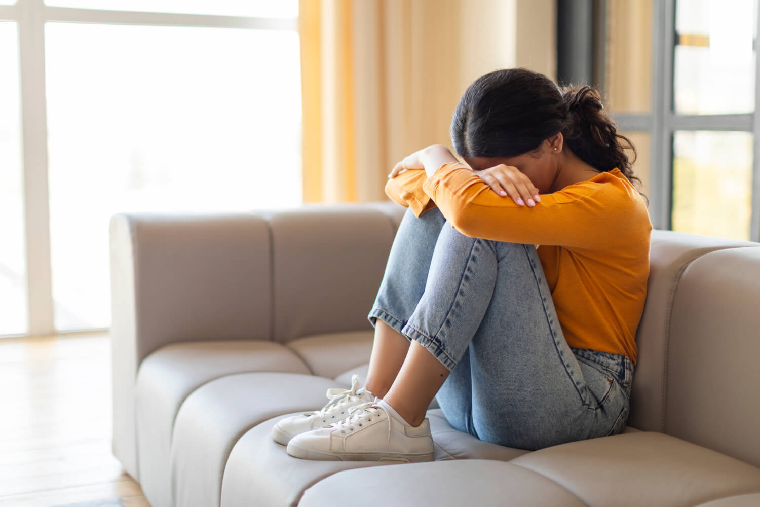 Young woman with head down, knees up, on couch.