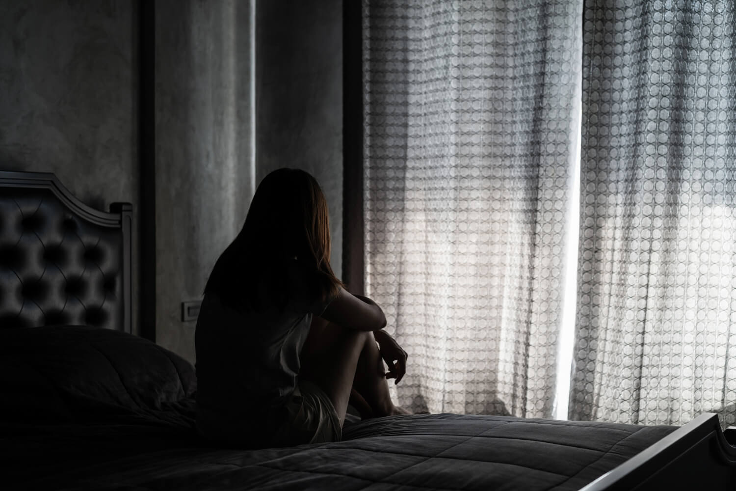 Silhouetted woman on bed in dimly lit room.