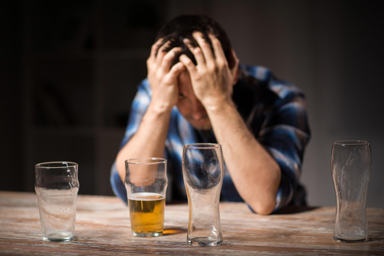 Man holding head, four empty beer glasses.