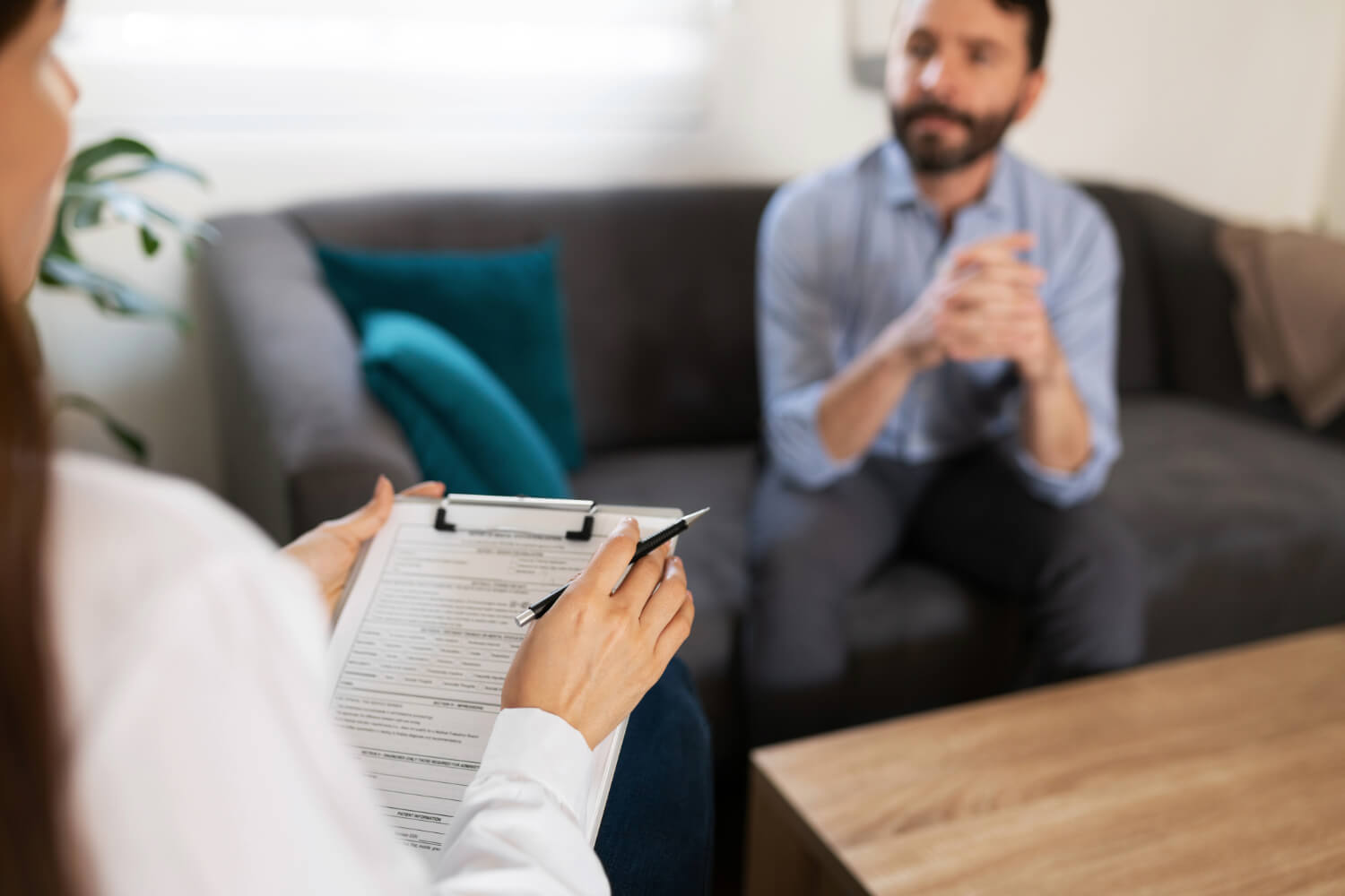 Therapist with clipboard, male client in background.