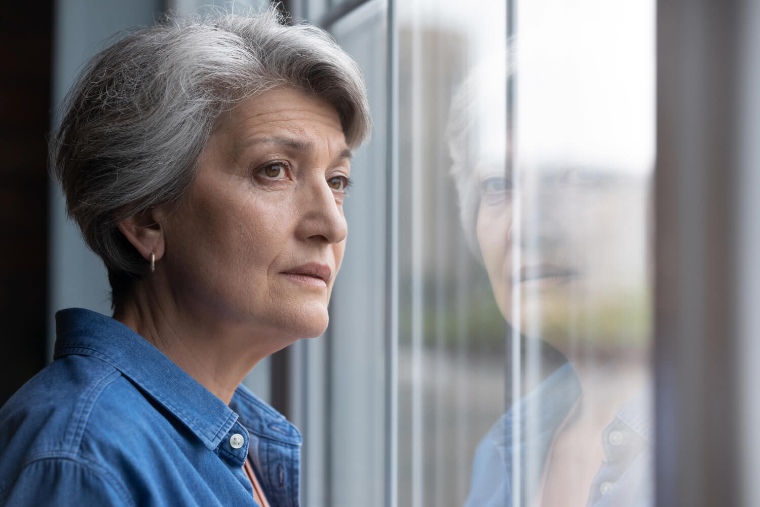 Elderly woman gazing out window.