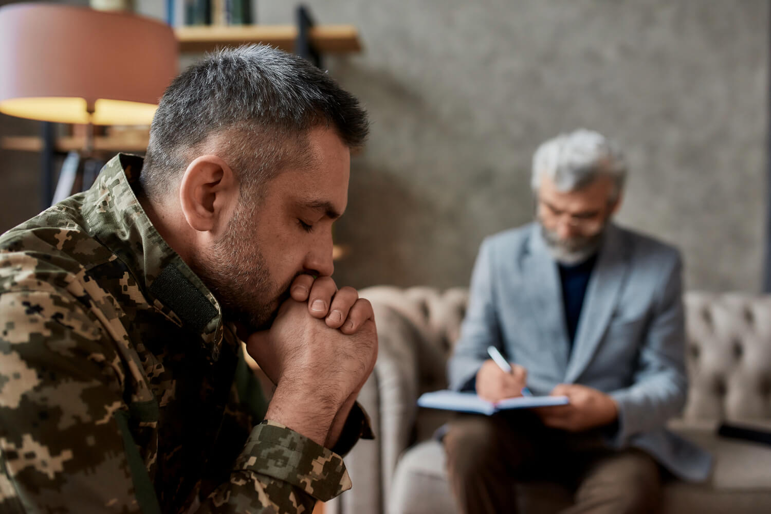 Man in military uniform, hands clasped, in therapy session.