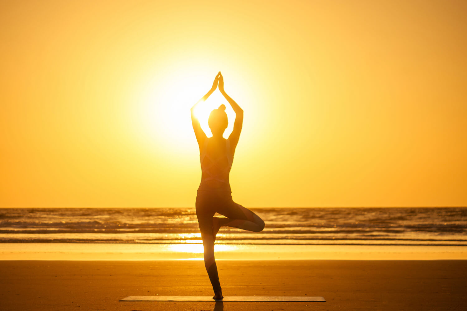 Woman practicing yoga on beach at sunrise