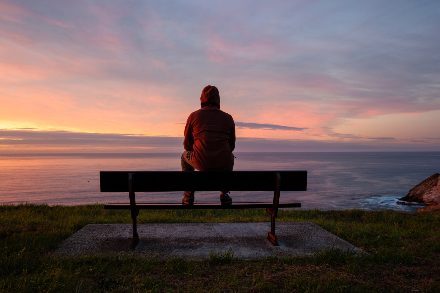Person sitting on bench overlooking ocean at sunset.