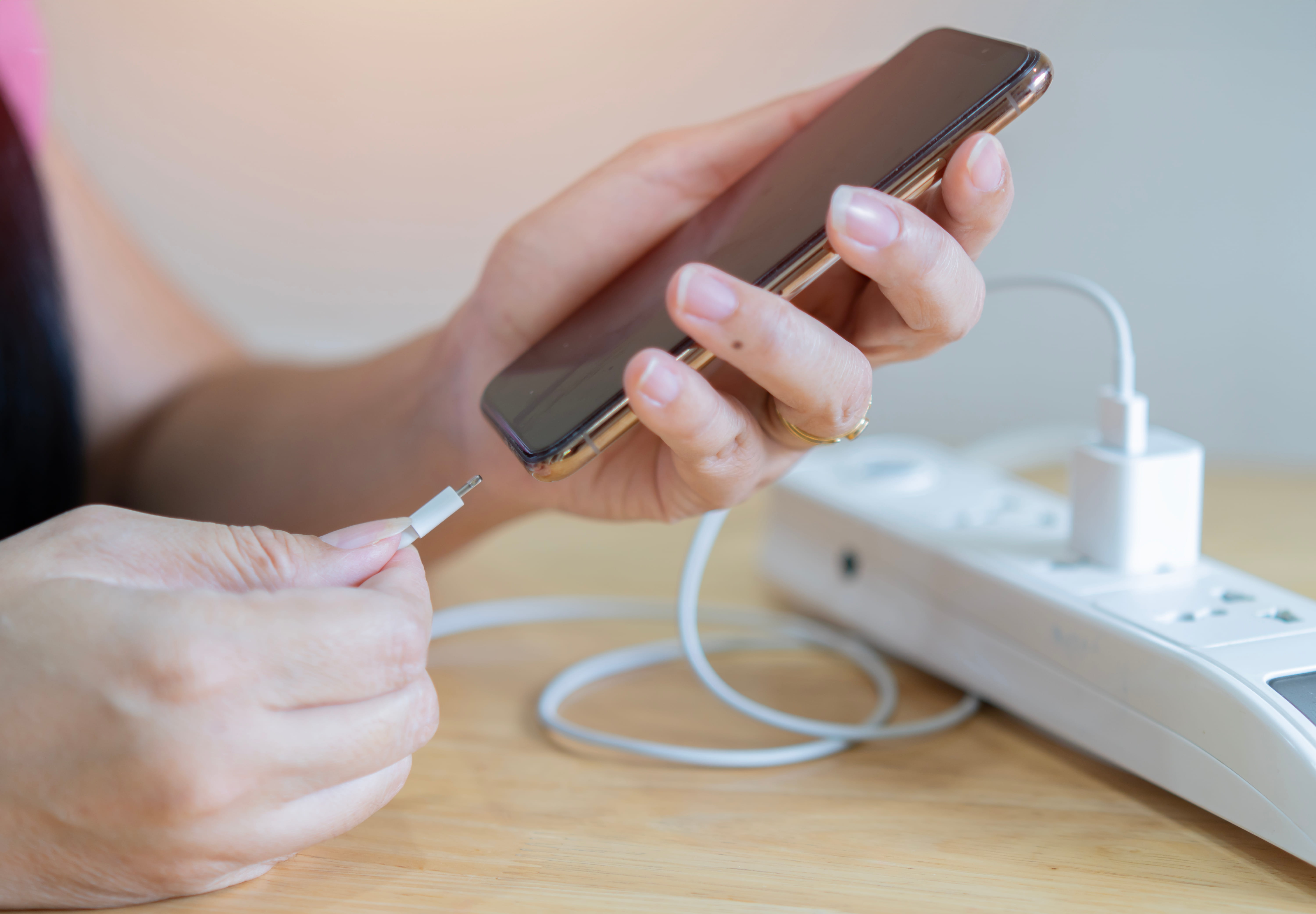 Person plugging a charging cable into a smartphone next to a power strip