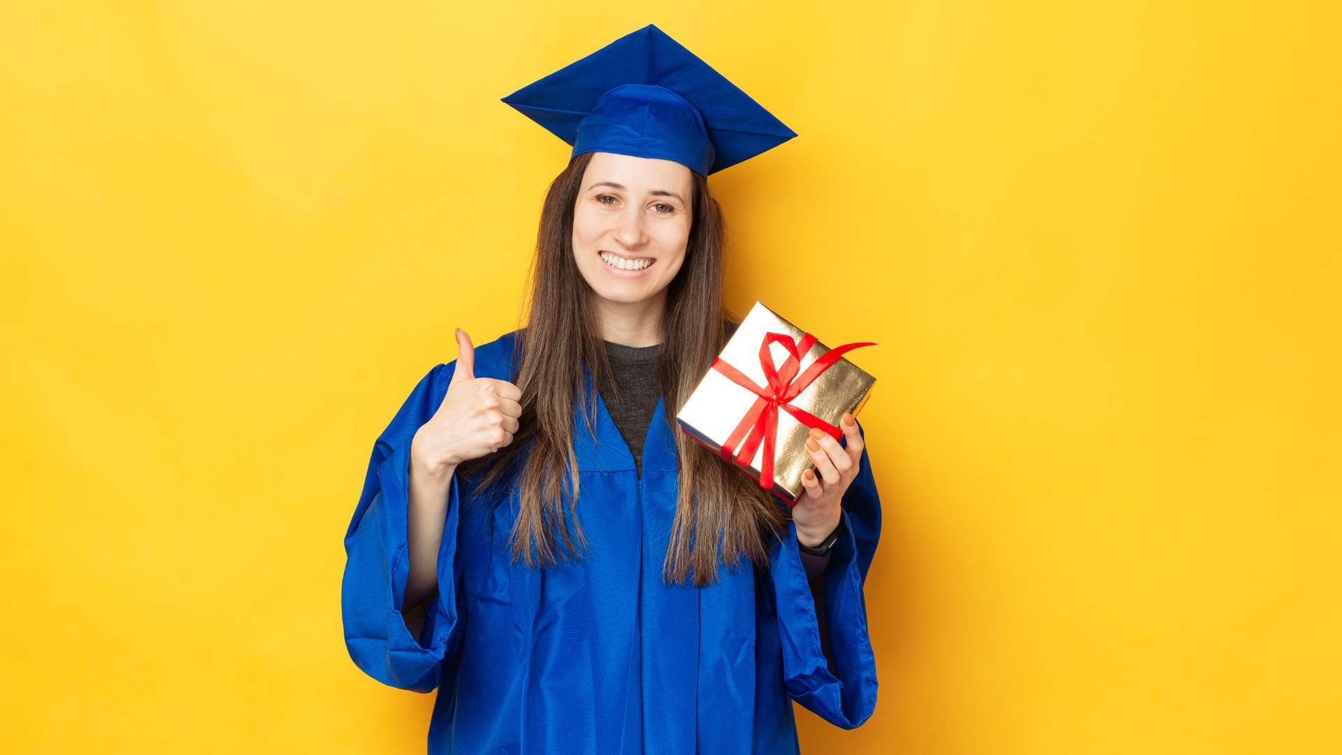 Smiling graduate in a blue cap and gown holding a wrapped gift