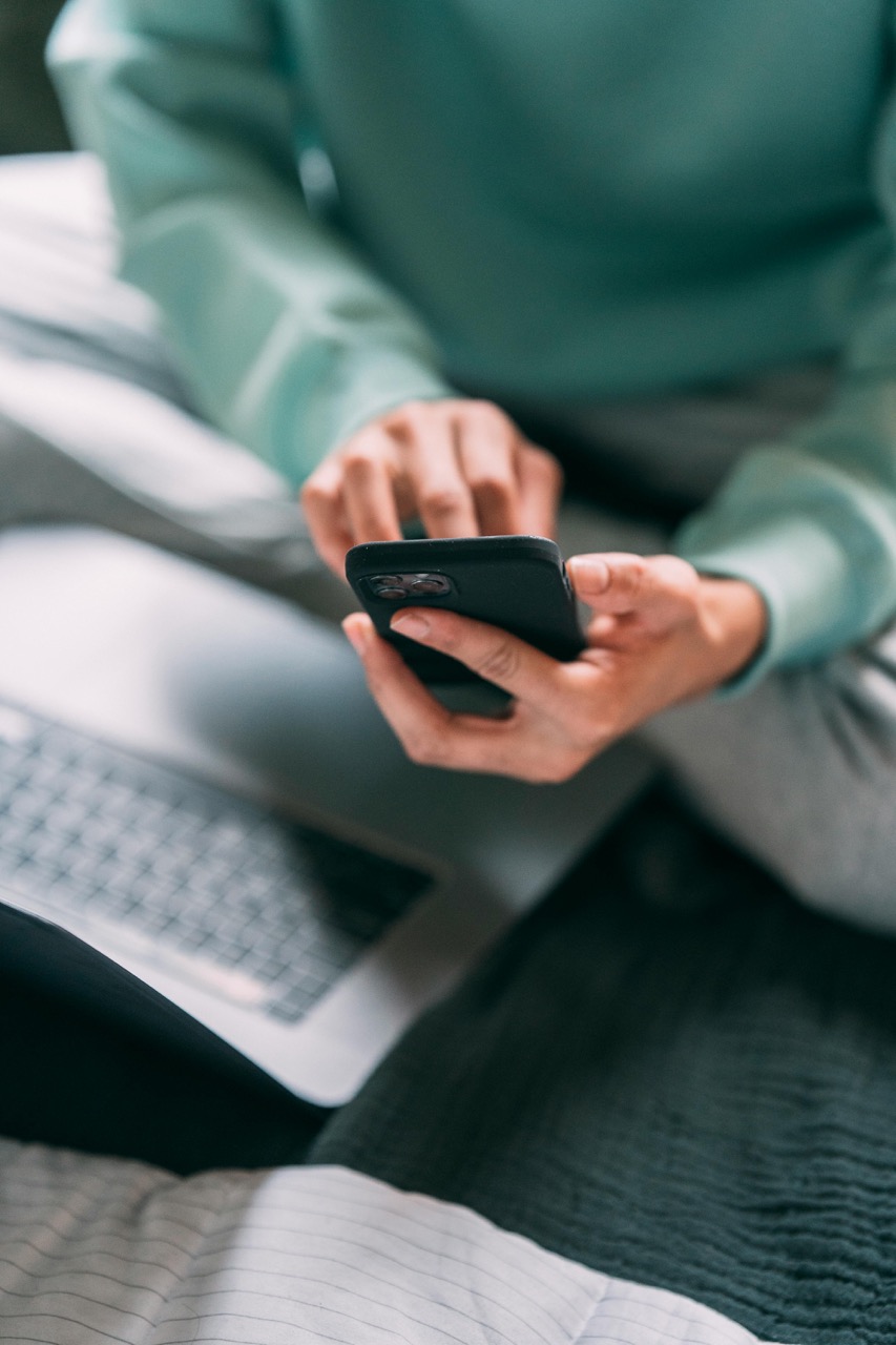 Person sitting with a laptop while using a smartphone