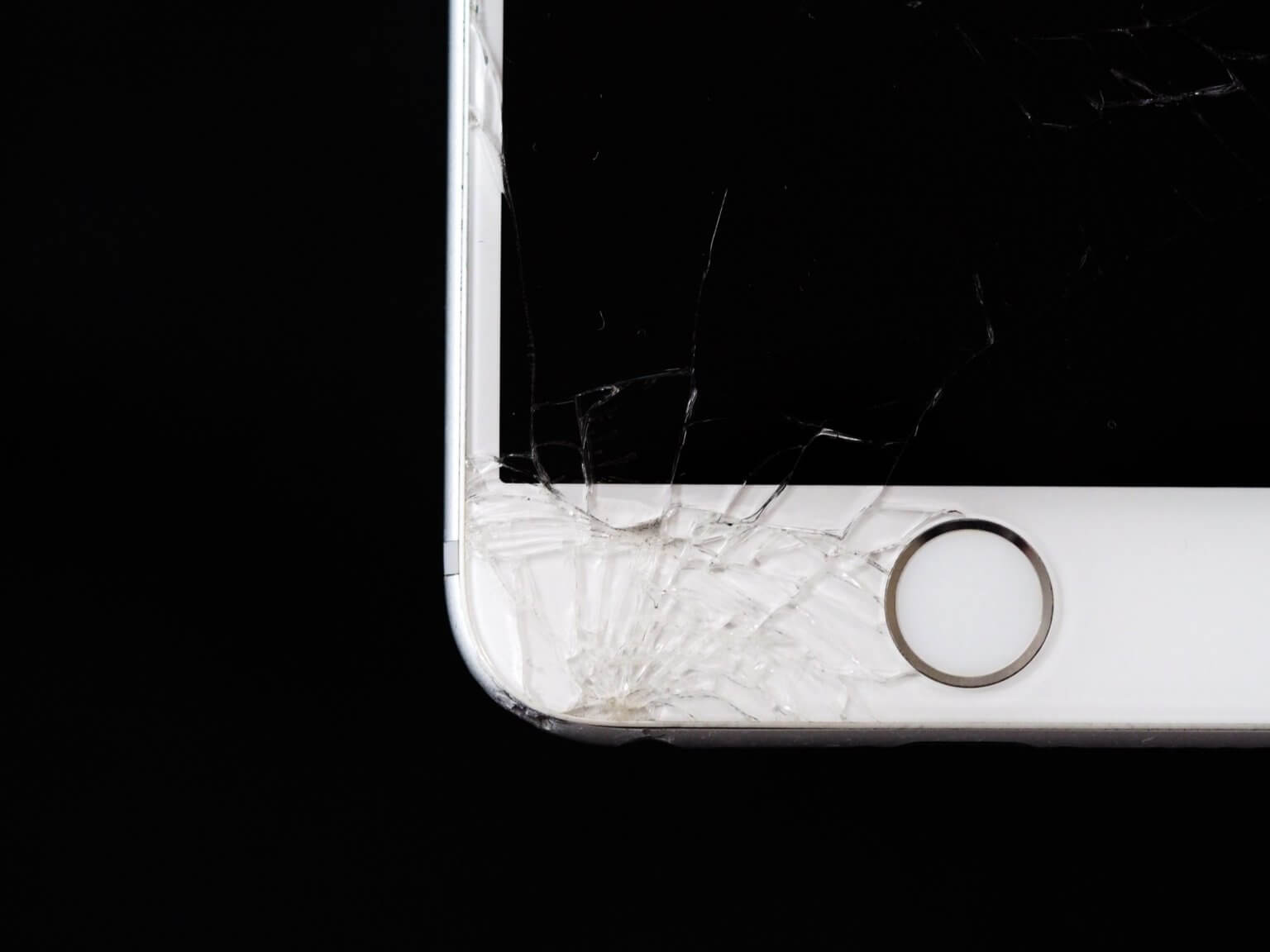 Cracked screen corner on a white iPhone with a home button