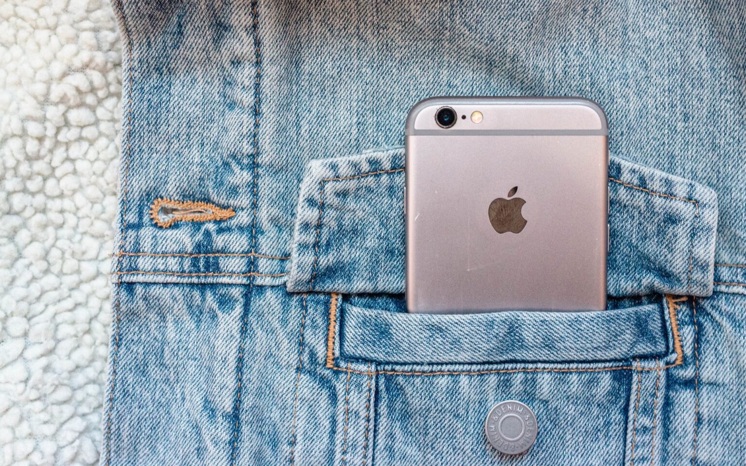 Rose gold iPhone tucked in the pocket of a denim jacket