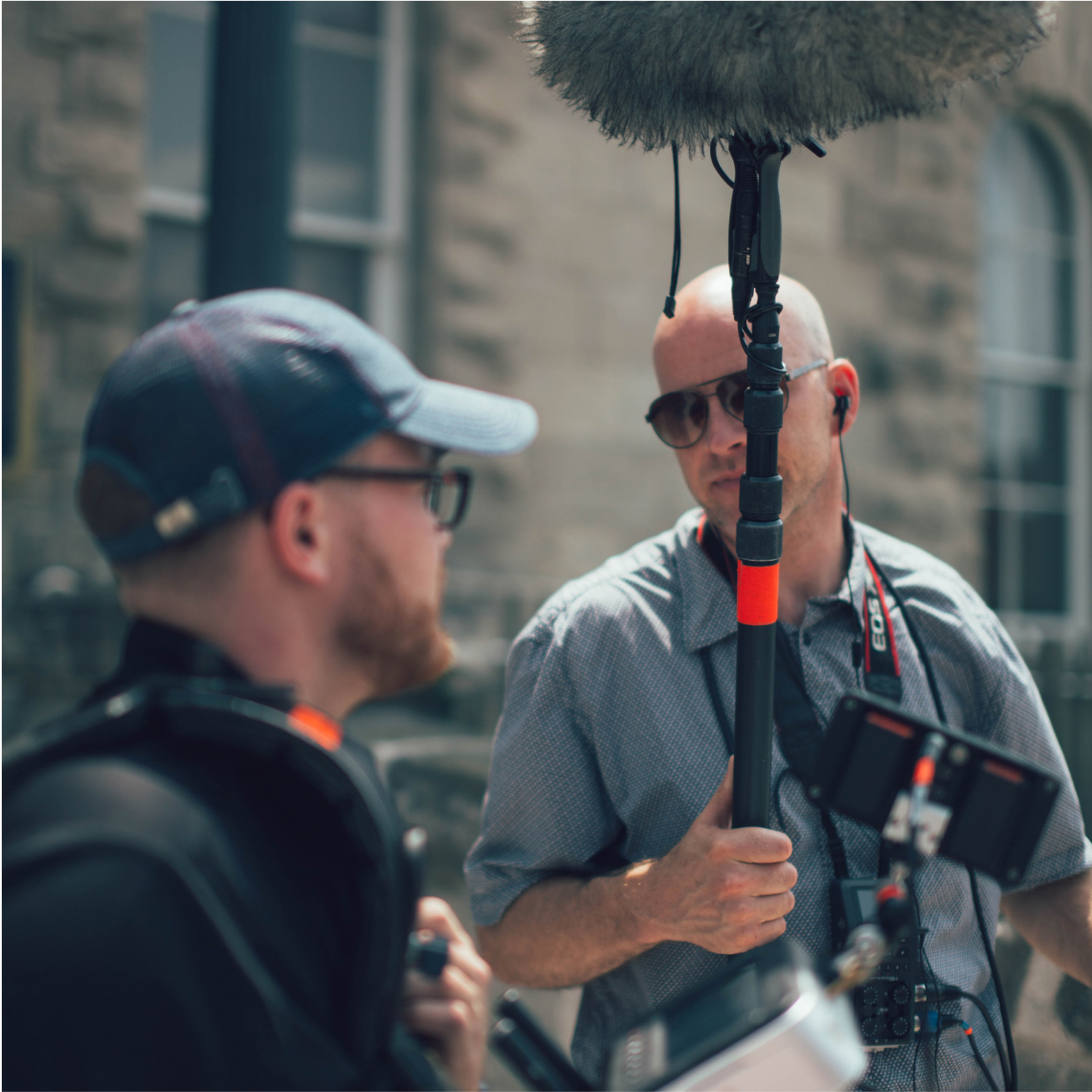 Two men holding camera equipment, talking.