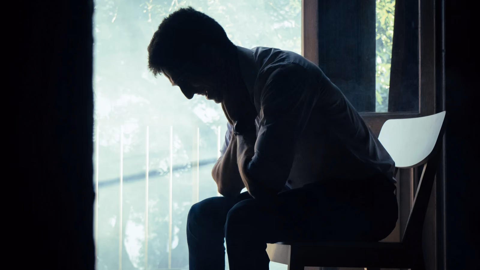 Un uomo è seduto da solo in un ambiente interno malinconico, la cui sagoma si staglia contro una finestra luminosa, immerso nei suoi pensieri. — Kari Alfonso – Pexels