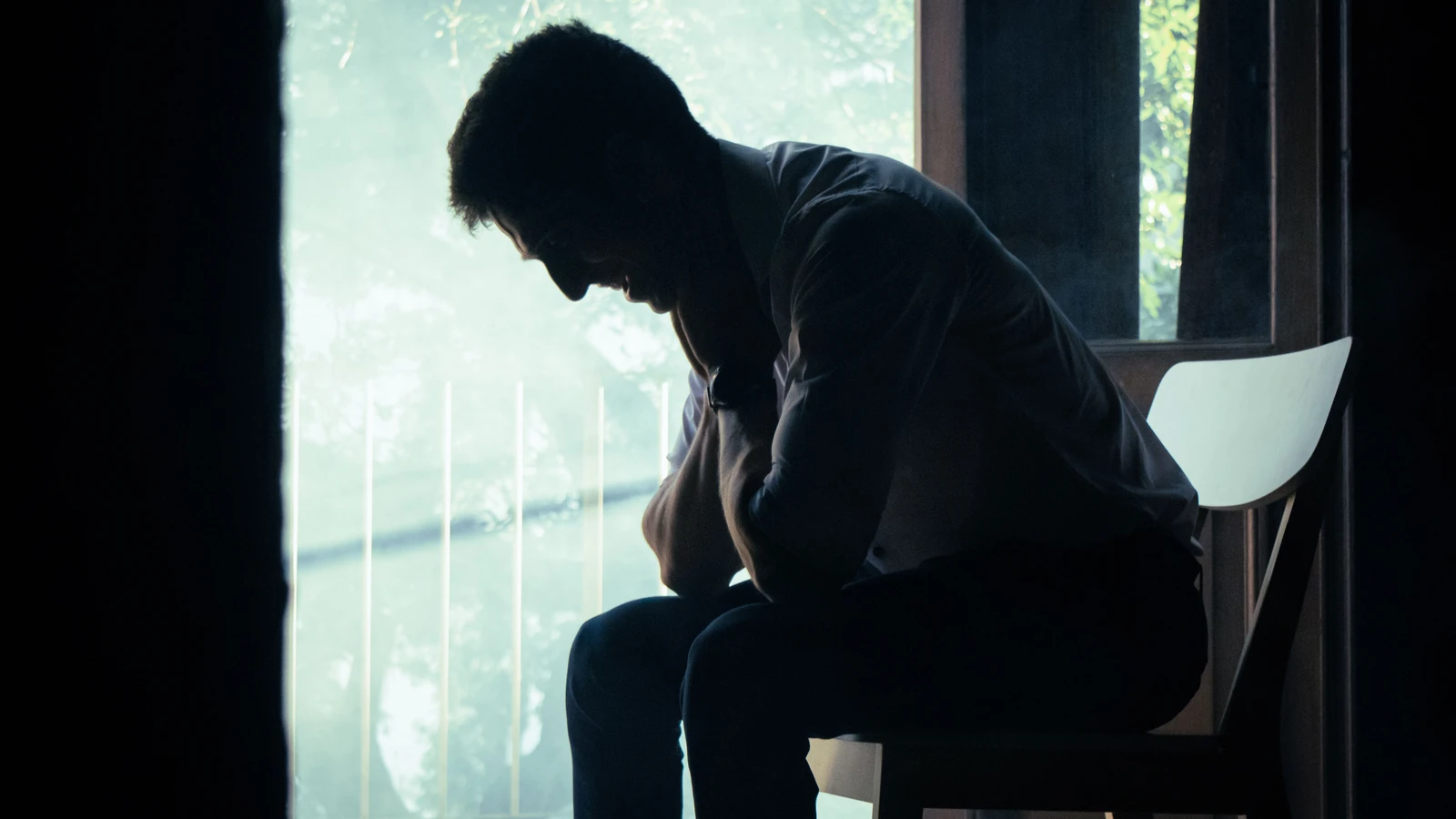 Un uomo è seduto da solo in un ambiente interno malinconico, la cui sagoma si staglia contro una finestra luminosa, immerso nei suoi pensieri. — Kari Alfonso – Pexels