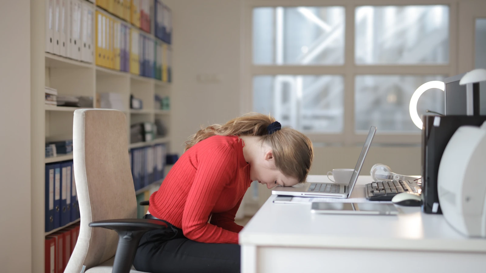 Donna in camicia rossa a maniche lunghe seduta su una sedia mentre lavora al laptop