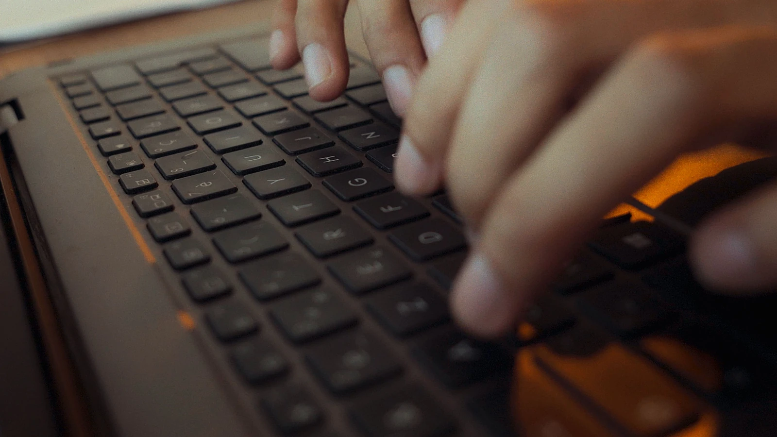 Primo piano di mani che digitano sulla tastiera di un computer portatile con luci soffuse in un'ambientazione algerina.