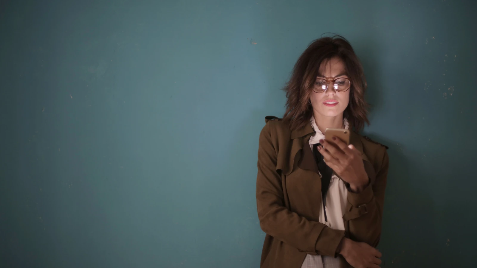 Donna appoggiata contro la parete verde acqua mentre usa il telefono cellulare — Andrea Piacquadio – Pexels