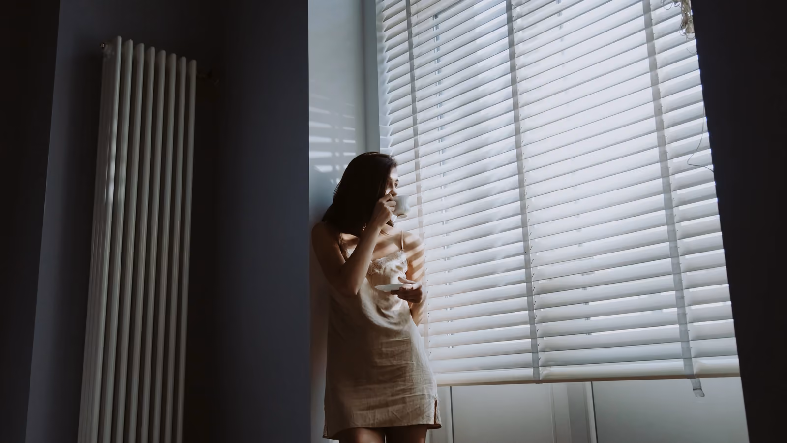 Una donna nella dolce luce del mattino è accanto alla finestra, tiene in mano una tazza e un piattino, assaporando un momento di pace. — cottonbro studio – Pexels