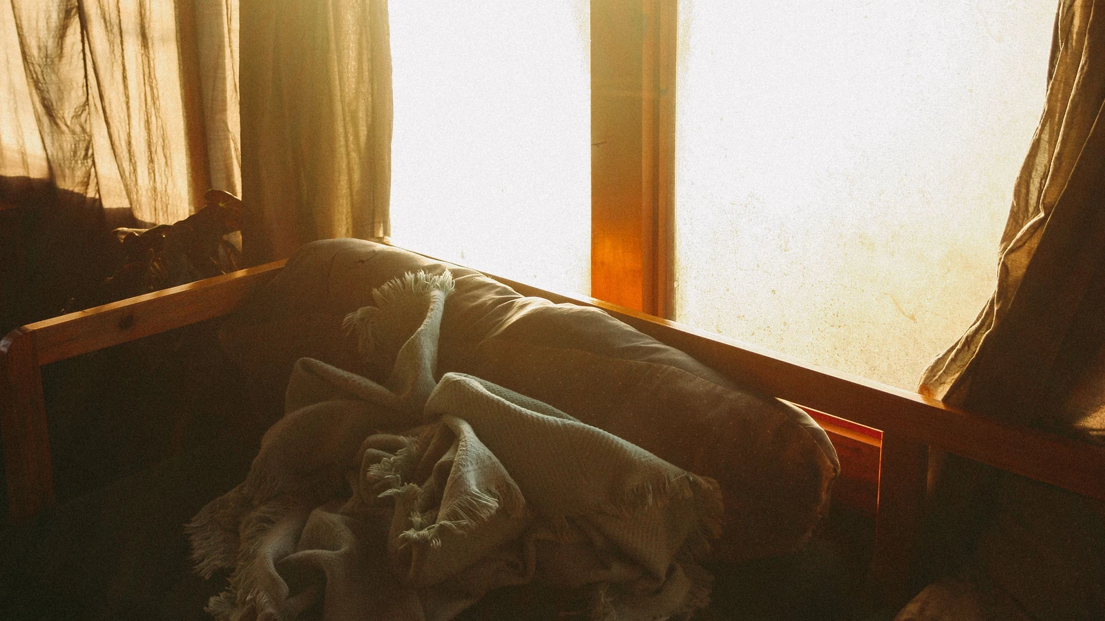 Scenario interno caldo e accogliente con la luce del sole che filtra da una finestra su un divano e una coperta.