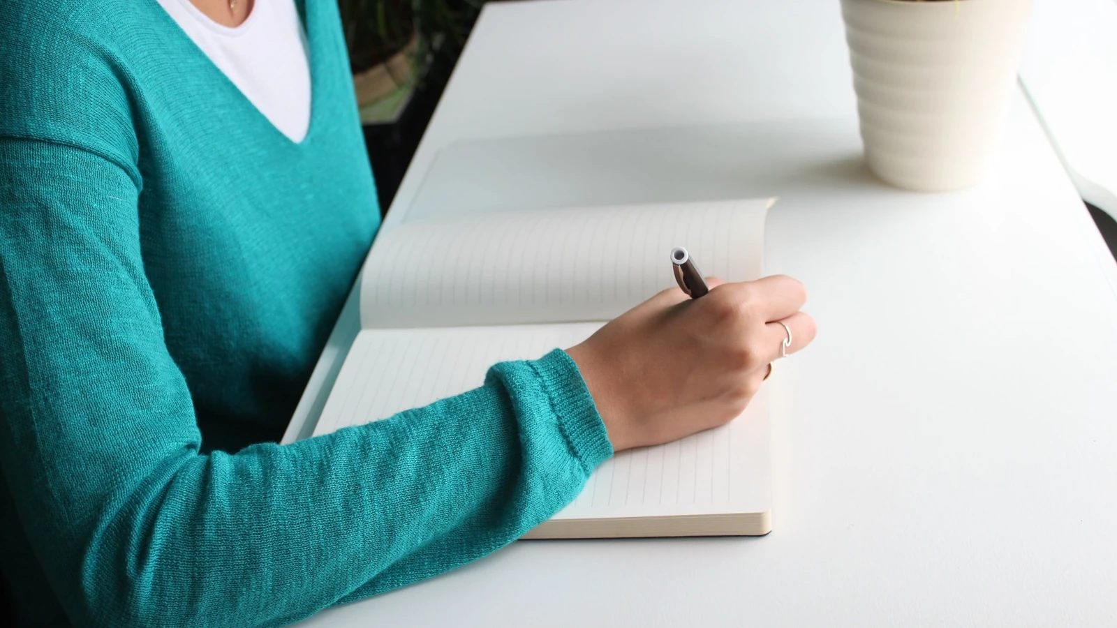 Una donna che scrive in un quaderno a una scrivania bianca minimalista, enfatizzando la produttività.