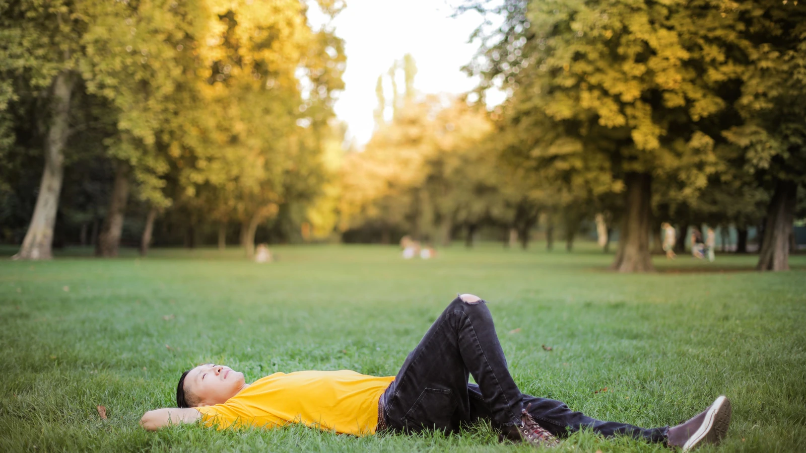 Foto dell'uomo in maglietta gialla e jeans neri sdraiato sul campo di erba verde